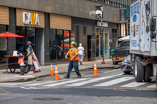 Manhattan, New York, NY, USA - July 8th 2022: Construction worker in orange west and helmet closing a street with traffic cones