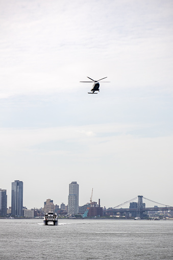 Manhattan, New York, NY, USA - July 8th 2022: Helicopter and ferry approaching the pier area at the end of East 35th Street with high rise buildings on the Queens shore in the background