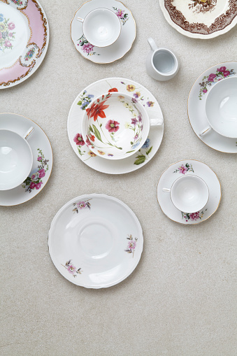 Variety of porcelain coffee and tea cups and small plates with ornaments on a modern granite table, top view with a copy space