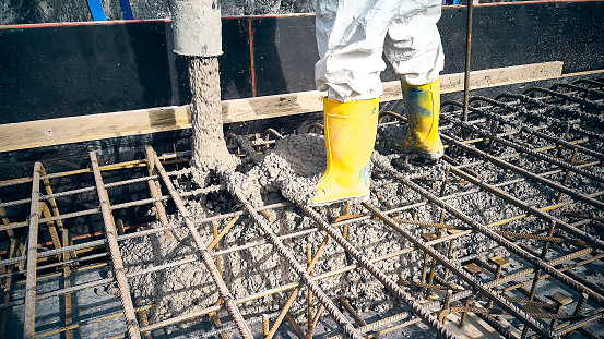 Construction worker dressed in uniform pour a concrete to formwork. Cement works on a construction site. Contractor is casting concrete using concrete pump tube
