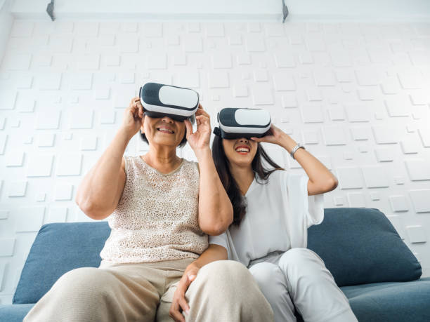 Asian young woman, happy daughter and her mother, old senior female wearing VR glasses, enjoy 3d game online together in white room. Mom and daughter with reality virtual technology lifestyle concept. la joven asiática, la hija feliz y su madre, una anciana mayor con gafas de realidad virtual, disfrutan del juego en 3d en línea juntos en una habitación blanca. mamá e hija con concepto de estilo de vida de tecnología virtual de realidad.