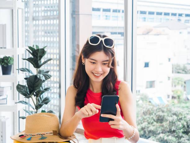 istock Young beautiful smiling Asian woman holding and using smart mobile phone, looking at screen. Happy Asian female wearing pink sleeveless, sunglasses, searching and planning for travel summer trip. 1416437515