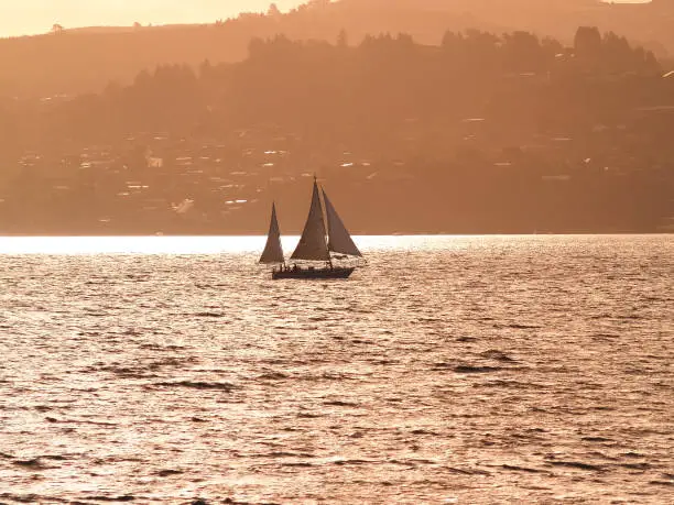 Silhouette distant hills and yacht sailing in under red sky at sunset on Lake Taupo, New Zealand.