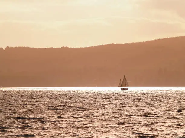 Silhouette distant hills and yacht sailing in under red sky at sunset on Lake Taupo, New Zealand.