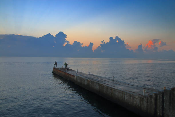 The photo was taken in the city of Odessa in Ukraine. The picture shows fishermen fishing from a concrete pier at sunrise.