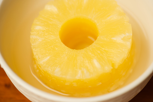 Glass of pineapple juice on wooden table.  Very shallow depth of field (focus on the front edge).