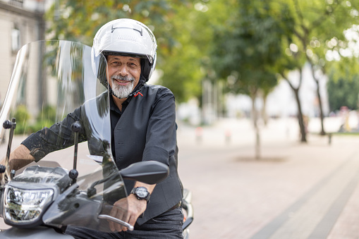 Mature man with crash helmet sitting on a motorcycle outdoors in city.