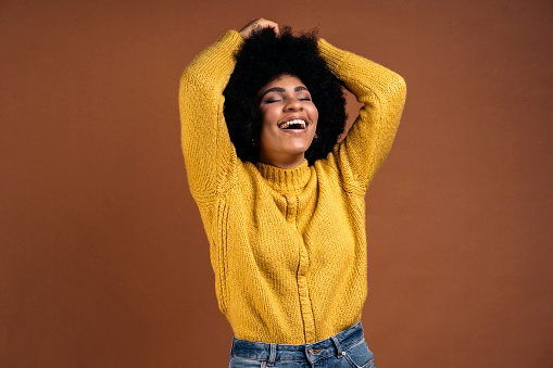 Smiley afro girl having fun in studio shot against brown background.