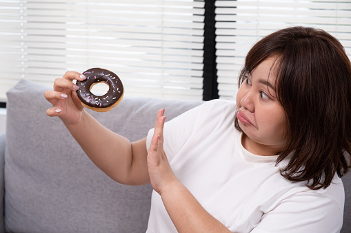 Young plus size Asian women stop herself from eating donut to control body weight during diet period. Healthcare and body weight control to prevent overweight, diabetes and obesity.Young Asian oversize women gain weight while eating donut, bread and snack and watching television on sofa couch. Junk food that can cause obesity and unhealthy for human body.Young Asian oversize women gain weight while eating donut, bread and snack and watching television on sofa couch. Junk food that can cause obesity and unhealthy for human body.Young Asian oversize women gain weight while eating donut, bread and snack while lay down and sleep at sofa. Junk food that can cause obesity and unhealthy for human body.