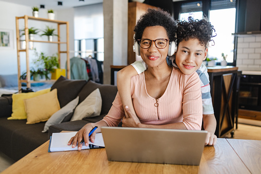 African-American mother is at home, she is working on the laptop and taking care of her son