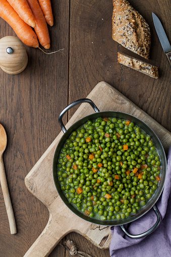 Green peas in a pan on a brown wooden kitchen table top, vegan food concept, top view with a space for copy