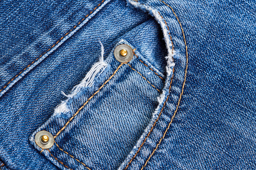 A blue denim jeans pocket with damages, seams, rivets and orange thread stitches