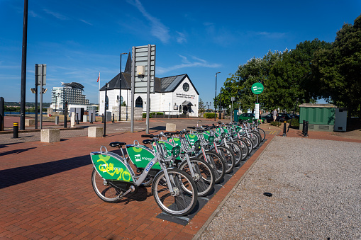 Cardiff United Kingdom Bike share bikes in docks by the waterfront operated by the Nextbike company under a local OVO brand. A church is in the background.