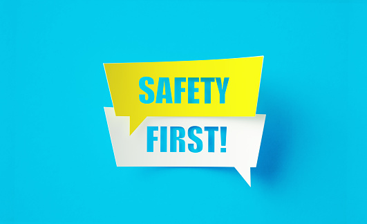 Safety first written cut out yellow and white speech bubbles sitting on blue background. Horizontal composition with copy space.