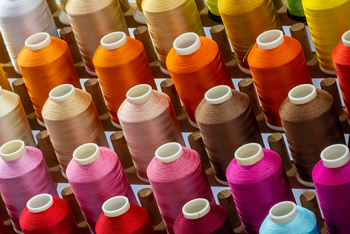 A close up image of a loosely arranged stack of reels of swing thread in a various colours against a plain white background. Shot with a shallow depth of field with focus on the bobbins in the foreground. 