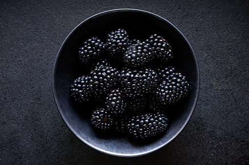 Fresh blackberries in a bowl on a black background, top view