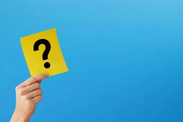 Photo of Question mark design. Hand holding note paper with question mark on blue background