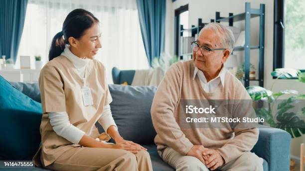 Young Asian Female Professional Caregiver Take Care Older Men Share A Story Together In Living Room At Home Stock Photo - Download Image Now