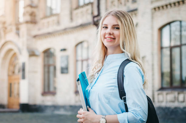 istock A blonde student girl is smiling and holding a folder and a notebook in her hands on a university background. Girl is taking exams at university 1416475587