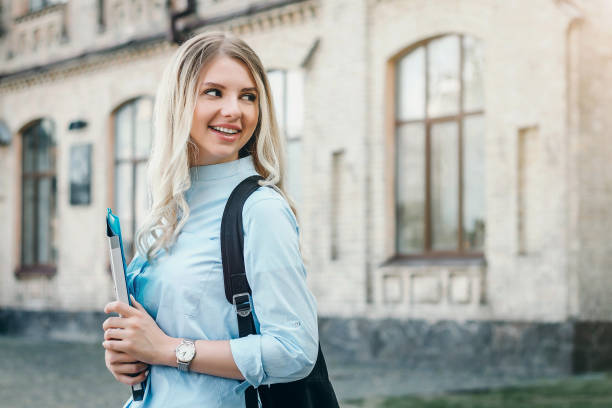 istock A blonde student girl is smiling and holding a folder and a notebook in her hands on a university background. Girl is taking exams at university 1416475616