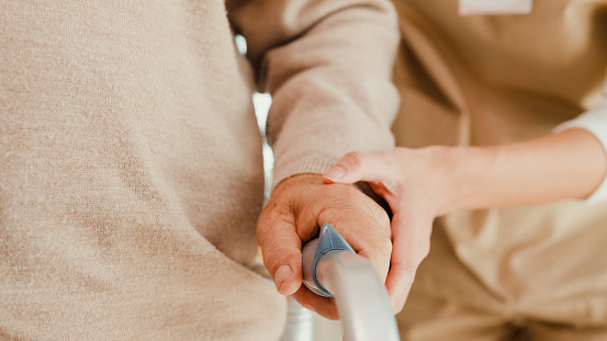 Close-up Young Asian female caregiver teach old male to walk use walker take care hold hand elderly patient at home. Assistance gentle girl support mature man, Rehabilitation healthcare concept.
