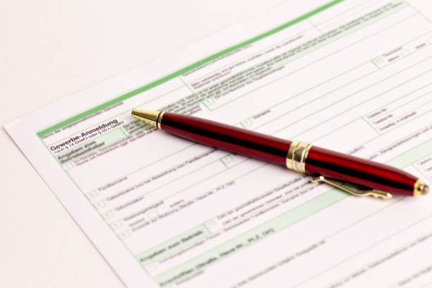 A ballpoint pen rests on top of a stack of documents ready for signing. The image is photographed using a very shallow depth of field with the focus being on the tip of the pen.