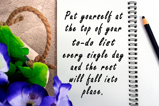 Motivational quote on notepad with potted plant background - Put yourself at the top of your to do list every single day and the rest will fall into place.