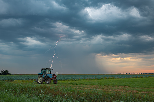 A thunderbolt of lightning strikes earth from a dramatic stormy sky behind a tractor in the green countryside.