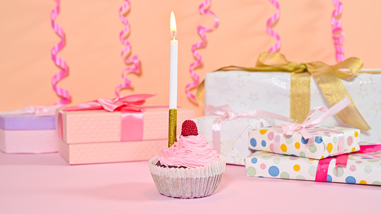 Birthday party gifts and cup cake with candle on pastel pink background.