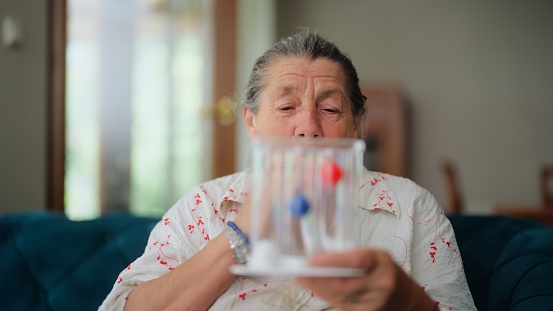 A senior woman is using a spirometer.