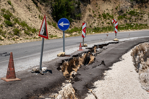 The asphalt road has slipped with the soil under it. There are warning signs on the road. There is a big rift in the asphalt.Road collapsed.