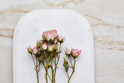 Dry miniature roses on a marble cutting board, on a modern granite table, top view with a copy space
