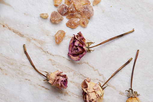 Caramelized sugar crystals on a modern marble table, with dry roses around, top view with a copy space