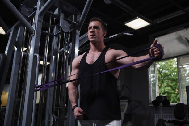 deportista entrenando con banda de resistencia en gimnasio - máquinas de ejercicios fotografías e imágenes de stock