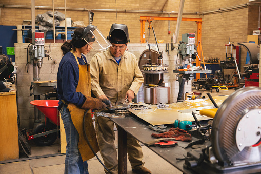 A young teenage high school female is practicing her welding skills while at school under a teacher's supervision. She is working in her high school shop class. Image taken on the Navajo Reservation, Utah, USA.
