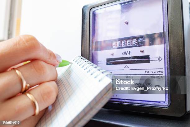 Womans Hands With Pen And Notepad Writes The Electricity Meter Readings At Home Stock Photo - Download Image Now