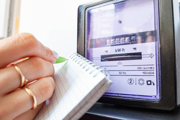 woman's hands with pen and notepad writes the electricity meter readings at home. - meter electric meter electricity fuel and power generation imagens e fotografias de stock