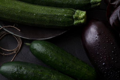 Fresh organic zucchini, eggplant and cucumber on a dark rustic table, dark mood vegan food preparation, with a free copy space all over the image