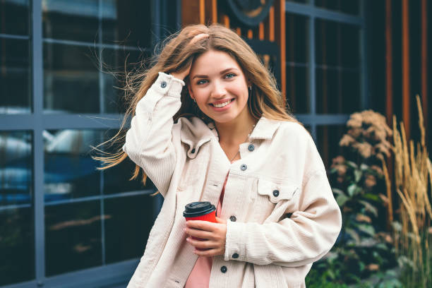 l’étudiante sourit et se promène dans la ville et se tient sur le fond d’un café, d’un restaurant. portrait d’une jeune femme dans la ville - corduroy jacket photos et images de collection