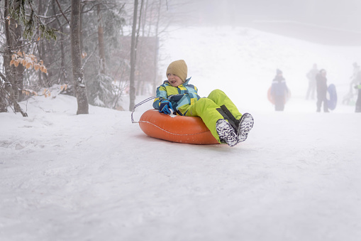 Little boy having extreme winter fun on sled. The boy is sledding down hill and yelling.\nNikon D850