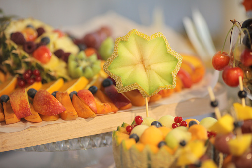 Fresh sliced multi-colored fruit carvings on buffet table.