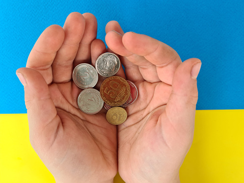 Ukraine and money and children's hand holds out handful of coins. International assistance to Ukraine in war investment and business.