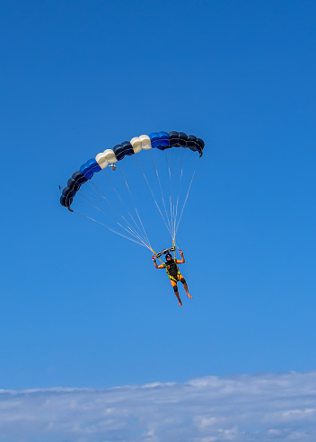 Paraglider pilot as silhouette with a white glider is flying in the clear blue sky, recreational and competitive adventure sport, copy space