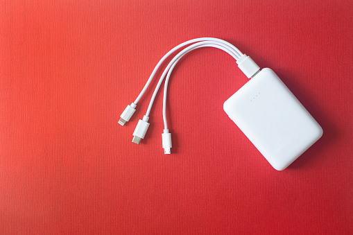 White power bank on red background. Powerbank with different connectors. External battery for different devices.