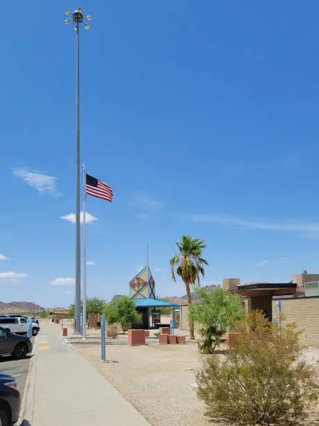 Parking and recreation area welcomes travelers with American flag on a tall flagstaff and a few heat tolerant green desert plants in pure xeriscaped landscape.
