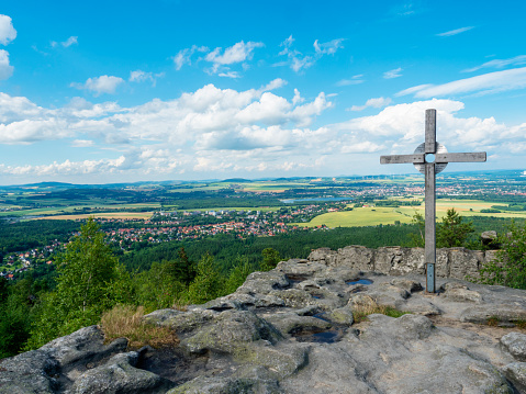 Tempelwand sandstone viewpoint with wooden cross next to hill Topfer near Oybin with view of Zittau town and Poland German borders in Zittauer Gebirge mountains, Saxony, germany. Summer sunny day.