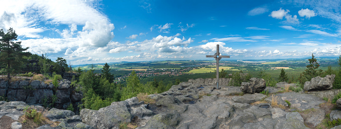 Panoramic view from Tempelwand sandstone viewpoint with wooden cross on hill Topfer, Oybin with view of Zittau and Poland German borders in Zittauer Gebirge mountains, Saxony, germany. Summer sunny day.
