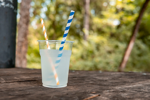 Image of a plastic cup of flavored water with two straws on a table in the park