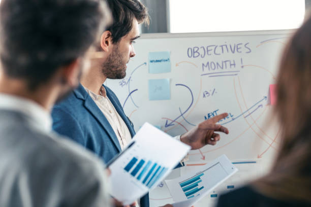 istock Handsome businessman pointing at white blackboard and explain a project to her colleagues on coworking place. 1416553841