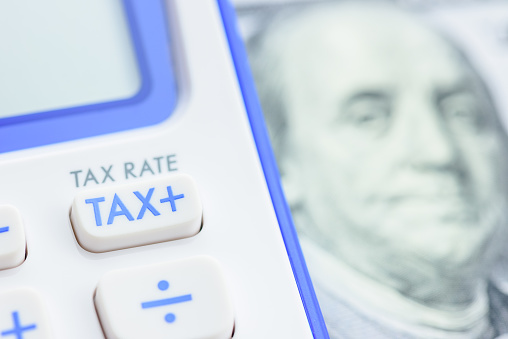 Income and payroll tax calculation, financial concept : TAX button on a calculator and 100 US dollar banknote. The image depicting a tax calculation that applies to both goods and services at the same tax rate.